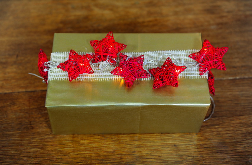 Pacchetto di Natale con carta regalo, nastro di juta e stelle luminose